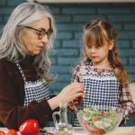 A senior woman and little girl making a fresh salad in the kitchen, enjoying quality time.